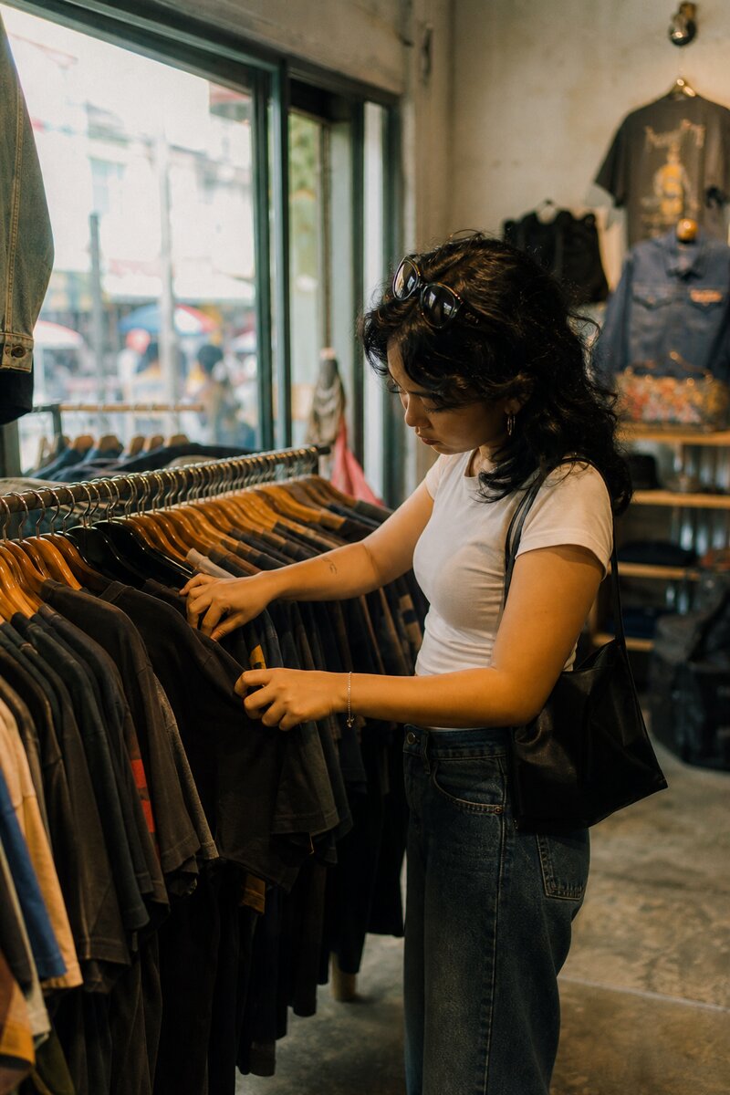 A shopper flipping through a rack of vintage denim and band tees in a Manila thrift boutique