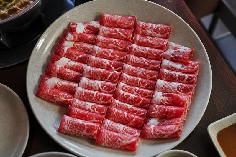 A platter of thinly sliced, beautifully marbled raw beef rolled and arranged in neat rows, ready for shabu-shabu