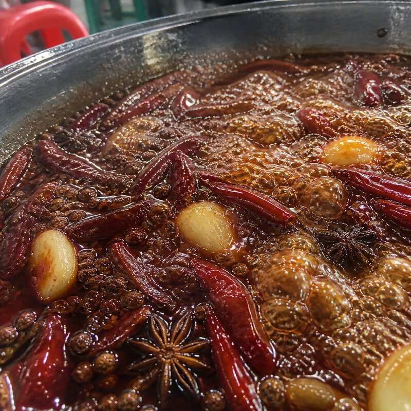 Close-up of a spicy Sichuan mala broth boiling with dried chilies, peppercorns, and floating aromatics in a hotpot