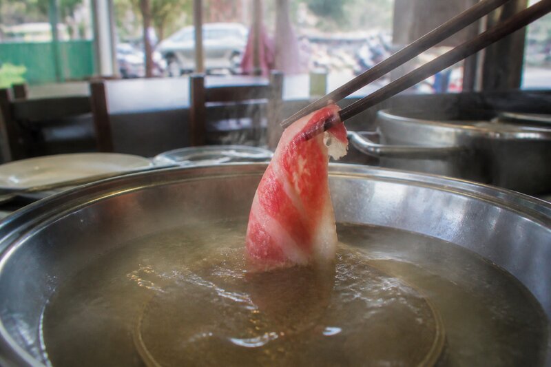 A pair of chopsticks swishing a thin slice of beef through a clear simmering broth in a hotpot
