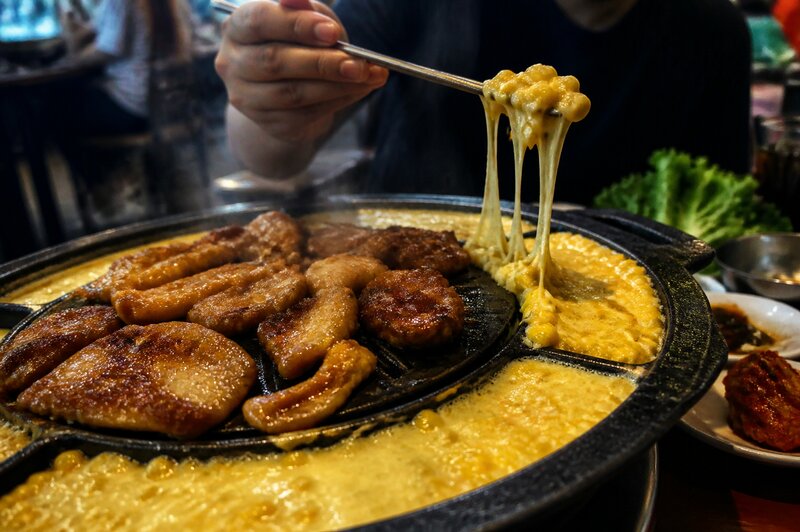 A cast-iron ring of bubbling corn cheese melting beside grilling meat at a Korean BBQ table