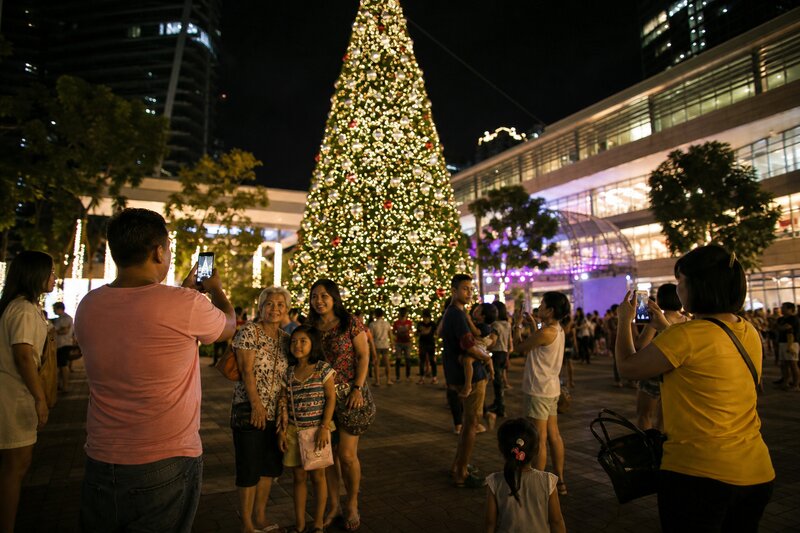A giant illuminated Christmas tree towering over a Metro Manila plaza with families gathered below