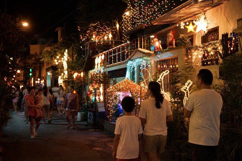 A residential street with houses covered in elaborate Christmas lights and figures, visitors walking through