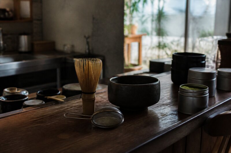 A minimalist matcha slow-bar counter with a chasen whisk, sifter and stone bowl