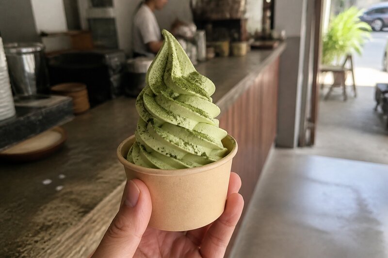 A swirl of green matcha soft-serve ice cream in a cup topped with matcha powder