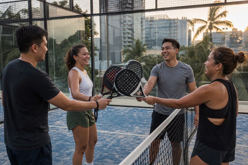 Four players laughing and tapping rackets together after a doubles padel match