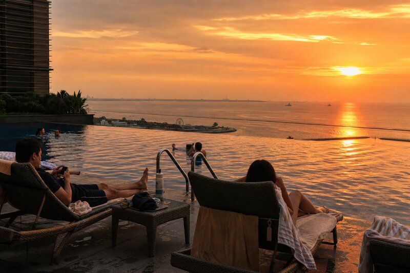 Guests relaxing at a bayfront hotel infinity pool as the sun sets over Manila Bay