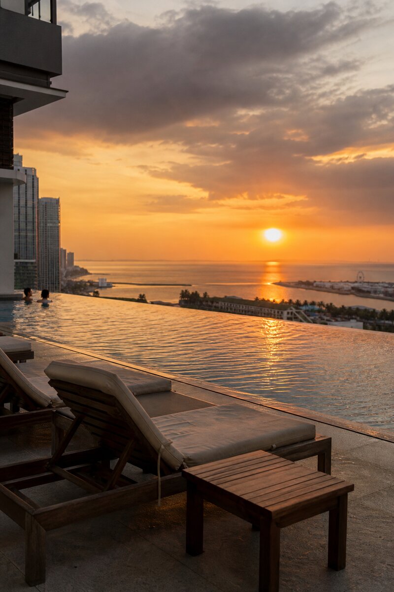 Rooftop infinity pool overlooking Manila Bay at golden hour, loungers along the water's edge