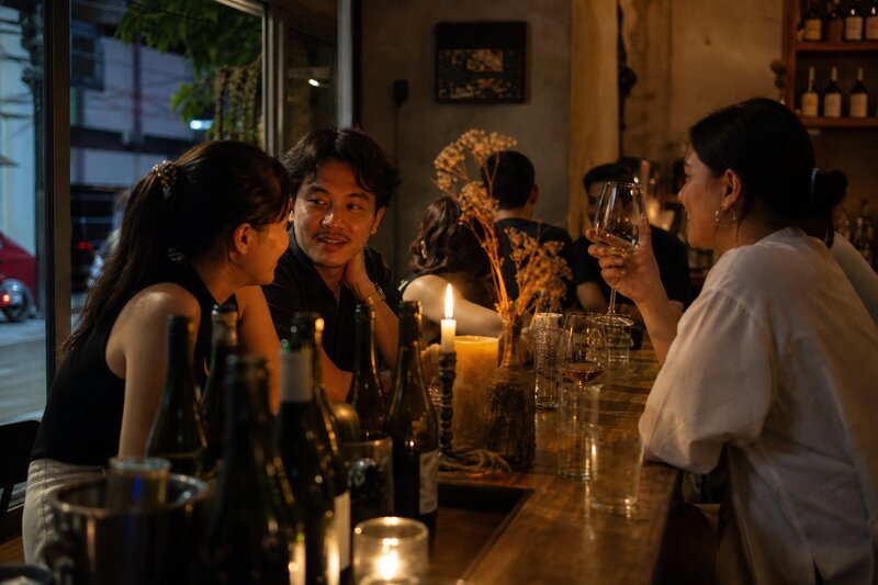 A candlelit natural wine bar at night with people chatting over glasses, warm intimate low lighting