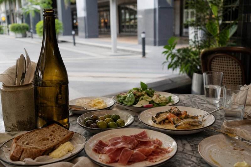 A spread of European-style small plates and a bottle of natural wine on a marble bistro table