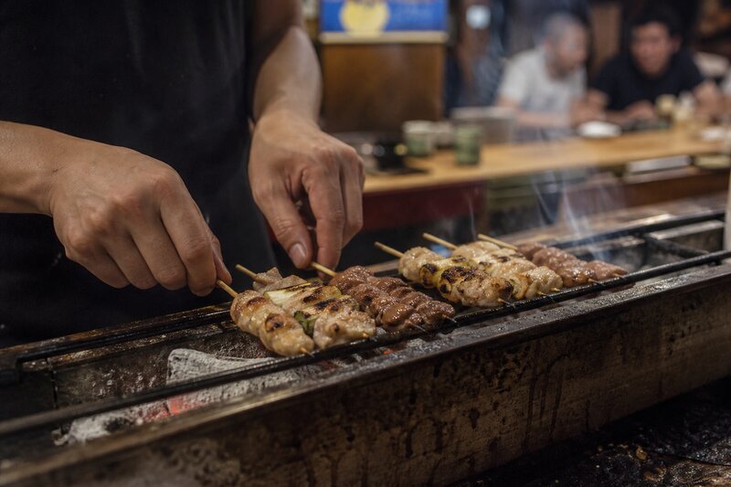 Skewers of yakitori grilling over glowing binchotan charcoal at an intimate counter