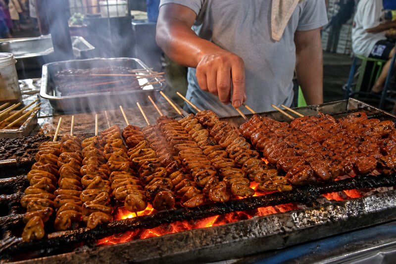 Charcoal-grilled Filipino street-food skewers -- isaw and barbecue -- sizzling over a glowing grill at a night market cart