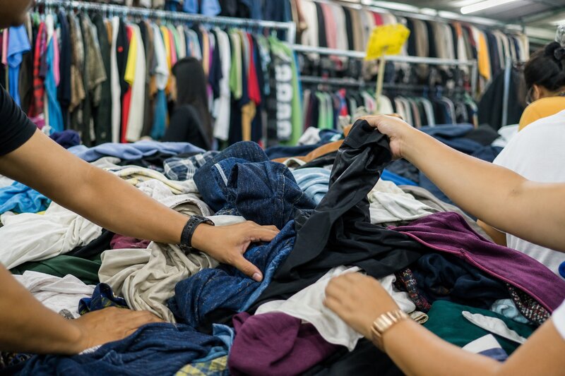 Hands digging through packed racks of secondhand clothes at a Manila ukay-ukay